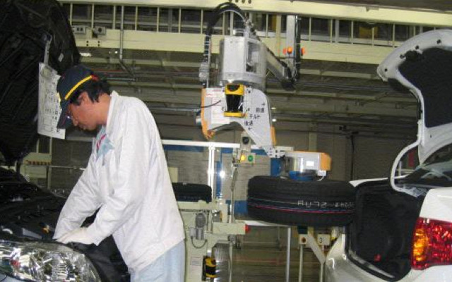 自動車の組立工場においてスペアタイヤを自動車のトランクに搭載するロボット