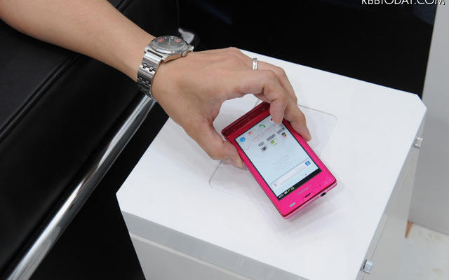 スマートフォン「AQUOS PHONE f SH-13C」（シャープ製）と、ワイヤレス充電器「ワイヤレスチャージャー 01」の組み合わせ。置くだけで充電を可能にした