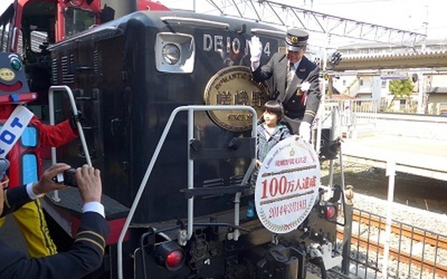嵯峨野トロッコ列車の年間利用者数が3月19日、初めて100万人を突破した。写真は記念のヘッドマークを取り付ける乗客代表ら