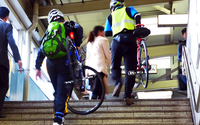 自転車を担いで階段を昇り、モノレール乗り場へと向かう参加者たち（11月30日、千葉モノレール実証実験「サイクル＆モノレール」）