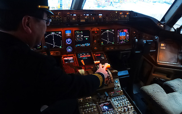 B777（JA8979）のコックピット。船越機長がスラスト・レバーに手をおく（羽田空港内JALメインテナンスセンター1（M1ハンガー））