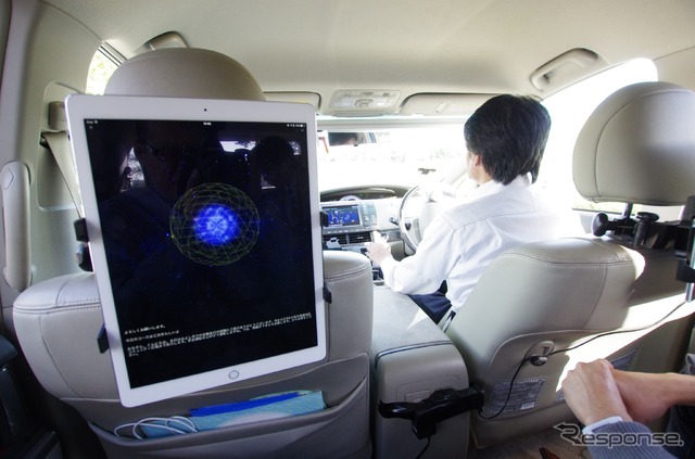 iPadのアプリとして稼働している「cocoro Drive」。色の付いた球体と、その回りのワイヤーフレームが感情を表現している。運転手は自動運転中だ。 《撮影 山田正昭》