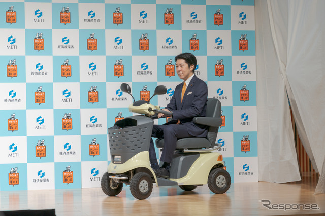 経済産業大臣政務官・佐藤啓氏が電動車いすに乗って登場。