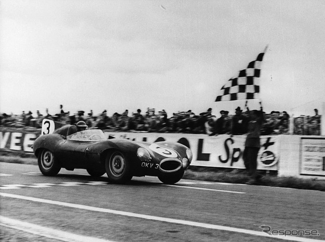 ランス12時間耐久でチェッカーを受けるジャガーDタイプ（1954年）。運転席はケン・ウォートン、組んだのはピーター・ホワイトヘッド。