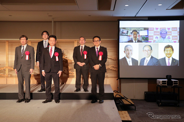 前列右より、経産省・江島潔副大臣、内閣府・三ツ林裕巳副大臣、国交省・渡辺学審議官。後列右より、東京大学 須田義大教授、内閣府SIP-adus・葛巻清吾PD。スクリーンは、右上から時計回りに、沖縄県北谷町・野国昌春町長、滋賀県東近江市・小椋正清市長、秋田県上小阿仁村・小林悦次町長、島根県飯南町・塚原隆昭町長、福井県永平寺町・河合永充町長。