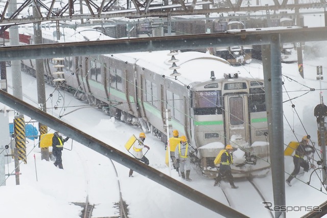 スノーダンプを担ぎ、除雪作業に入る人々。2022年2月22日、函館本線小樽駅。