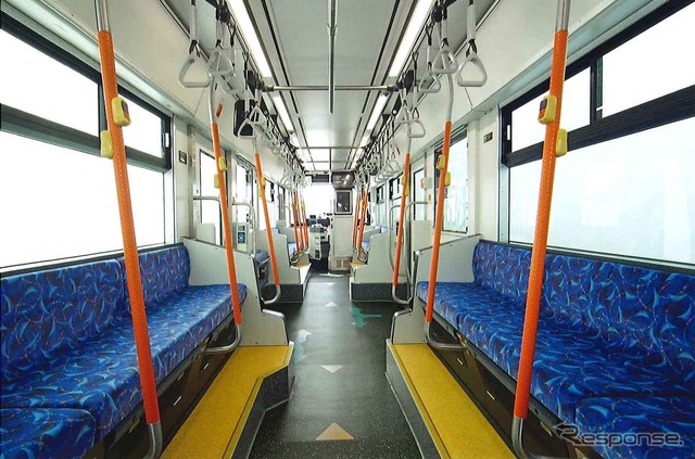 ライトグレーを基調とした6000形の車内。シートは帆船の帆や石畳、ステンドグラスといった長崎の風景をモチーフにしたブルー系。オレンジ色の握り棒を斜めに立てることで通路の空間を拡大している。照明は面発光LEDで、LED特有の眩しさを軽減。定員は62人。