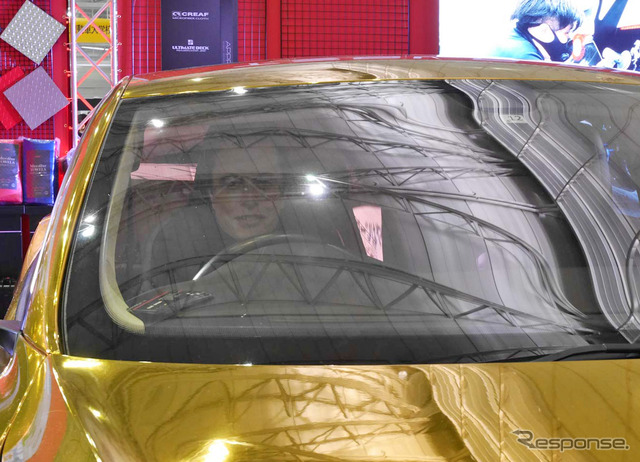 金色のクルマの運転席にはイーロン・マスクのマスク(お面)