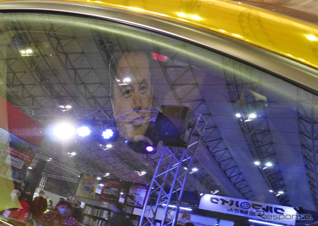 金色のクルマの運転席にはイーロン・マスクのマスク(お面)