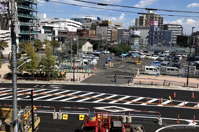 引き込み線レガシーの上、2階から所沢駅方面を望む(9月18日)。手前の赤いトラックの付近から通りを横切り、カーブしながら左奥の所沢駅に至る。灰白色の切妻の家屋は廃線後にできたと思われる