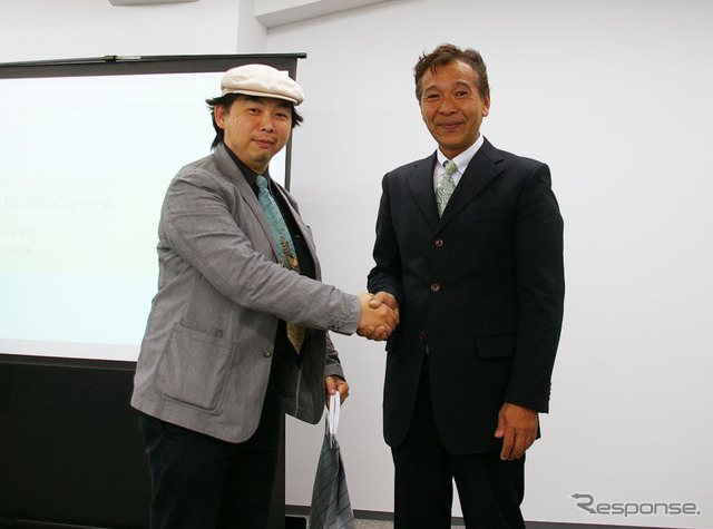 「たくさん充電したで賞」を頂戴し、大会委員長の増岡弘氏(右)と握手する筆者