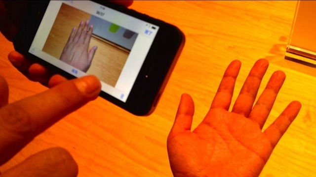 写真、電球色のライトのもとiPhone 5で撮影すると手がオレンジ色になってしまう。一方、iPhone 5sで撮影した画像を見ると自然な肌色となっている。
