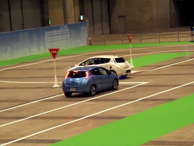 交差点でのシーン。青いクルマはドライバーがハンドルを握っている。白いクルマが自動運転車だ