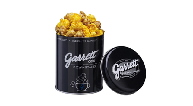 「メルセデス ミー オリジナル缶 シカゴミックス」800円片面には「Garrett cafe meets DOWNSTAIRS」の　ロゴとともに、カフェを連想させるコーヒーカップから溢れだすギャレット ポップコーンのイラストを配す。
