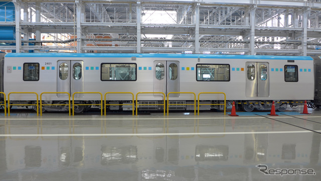 中間車(2401号)を真横から見る。側面は上部にアクアブルー(青)のライン、窓の位置には「スクエアドット」と呼ぶ青・緑・黄色・オレンジの四角を並べたカラーリングだ