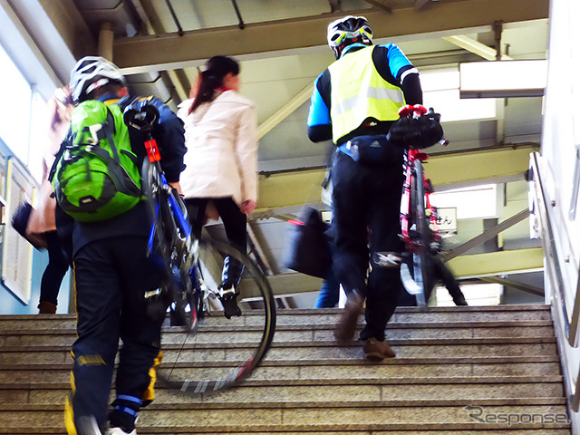 自転車を担いで階段を昇り、モノレール乗り場へと向かう参加者たち（11月30日、千葉モノレール実証実験「サイクル＆モノレール」）