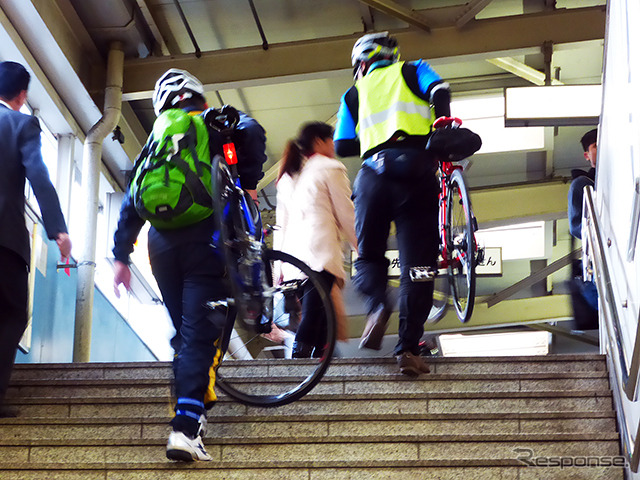 自転車を担いで階段を昇り、モノレール乗り場へと向かう参加者たち(11月30日、千葉モノレール実証実験「サイクル&モノレール」)