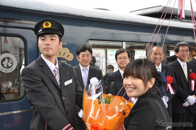 出発式でアテンダントの前田菜津美さん(右)から花束を受け取った運転士の矢野裕城さん(左)