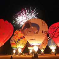 熱気球ホンダグランプリ2022最終戦、渡良瀬バルーンレース2日目夜に行われたファン向けイベント「バルーンイリュージョン」。バーナーを吹かして熱気球を光らせ、背後では打ち上げ花火が結構盛大に上がる。