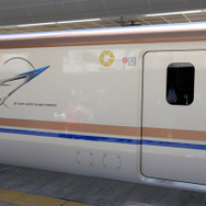 E7系の長野寄り先頭車、12号車の側面に描かれたシンボルマーク。車体肩と窓下に入った銅色が輝く