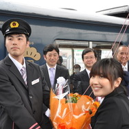出発式でアテンダントの前田菜津美さん（右）から花束を受け取った運転士の矢野裕城さん（左）