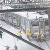 スノーダンプを担ぎ、除雪作業に入る人々。2022年2月22日、函館本線小樽駅。