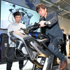 実際にヤマハ発動機がバイクの開発現場で使用するシミュレータ『MOTOLATOR』を世界初公開。デザイナーの渡辺さん（左）にレクチャーを受ける筆者・青木タカオ（右）