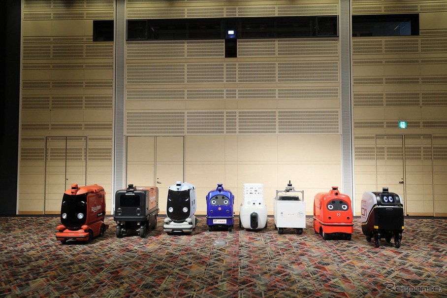 ロボットデリバリー協会各社の自動配送ロボット：向かって右から川崎重工業、ZMP、TIS、ティアフォー、日本郵便、パナソニック、本田技研工業、楽天グループ